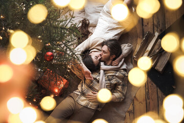 Kissing stylish love couple girl, guy lie on skin on floor in cozy wooden country house,chalet in winter forest.Celebrating new year eve.Gifts,family holiday.Romantic weekend.Decorated Christmas tree