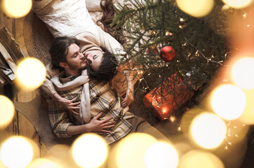 Kissing stylish love couple girl, guy lie on skin on floor in cozy wooden country house,chalet in winter forest.Celebrating new year eve.Gifts,family holiday.Romantic weekend.Decorated Christmas tree