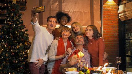 A group of multi ethnic. Portrait of Caucasian and African American black woman have a celebration dinner taking a selfie in party on Merry Christmas Eve Xmas on holiday at home. People lifestyle.