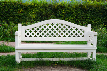 White bench in the park against the backdrop of a green hedge