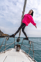 Woman standing on the nose of the yacht at a sunny summer day, breeze developing hair, beautiful sea on background