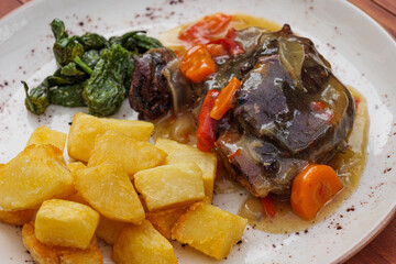 Homemade meat with sauce, carrots, peppers and potatoes on white plate.