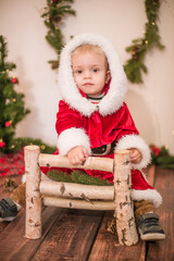 
Little cute boy dressed as Santa Claus in a room decorated for Christmas. Christmas and children