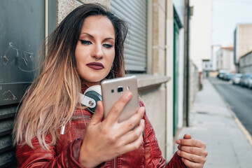 urban young woman with headphones and phone on the wall in the street