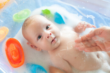 Baby bath time. Close-up detail view of mother bathing cute little peaceful baby in tub with water...