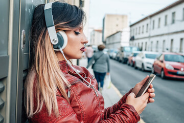 urban young woman with headphones and phone on the wall in the street