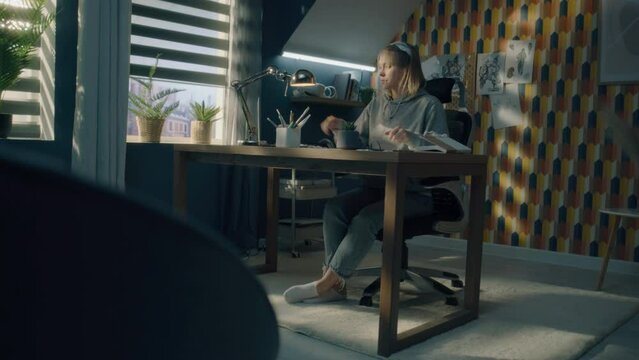 Young woman finishes off her work. Takes off her glasses and switches off the laptop and the table lamp. Home office concept. Creative designer. Sketching, work from home.