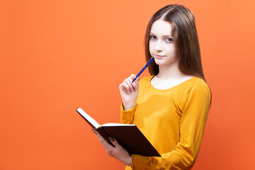 Winsome Young Blond Girl in Yellow Shirt Posing isolated on Orange Background Studio Portrait as People Lifestyle Concept While Writing Notes in Notebook