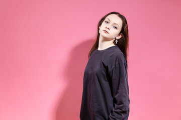 Portrait of Serious Blond Teenager girl in hoodie attentively looking at camera While posing with tilted head in studio Isolated on Pink Background
