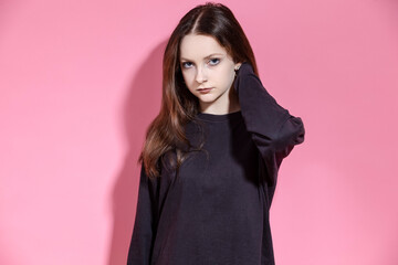 Portrait of Serious Blond Teenager girl in hoodie attentively looking at camera While posing with lifted hands in studio Isolated on Pink Background