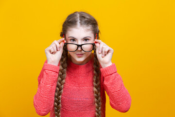 Intelligent Clever Winsome Caucasian Blond Girl In Warm Knitted Sweater Posing with Glasses and Lifted Hands While Staring at Viewer Against Yellow.