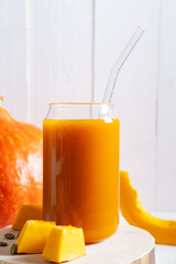 Pumpkin juice in a glass jar with a close-up tube on a wooden stand.