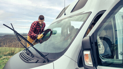 Young man cleaning camper van windshield with cloth outdoor