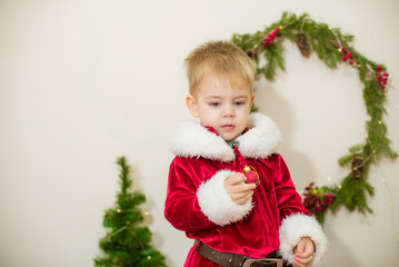 Little cute boy dressed as Santa Claus in a room decorated for Christmas. Christmas and children
