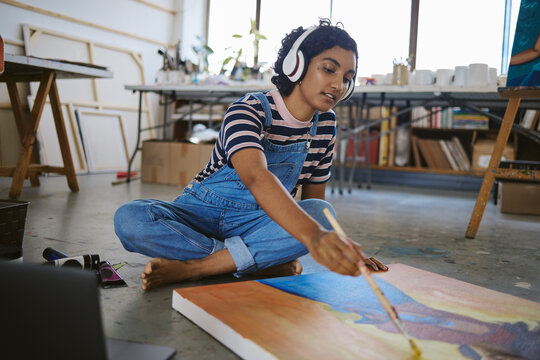 Music, painting and art with woman on floor of workshop studio working on creative, idea or vision on canvas. Relax, designer and goals with girl artist and headphones for peace, wellness or freedom