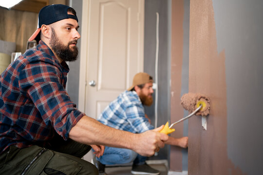 Young bearded workers painting wall in room with roller. repairs painting tools. repair, painting and home interior
