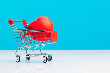 A mini shopping trolley with a red heart shape on a blue studio background. Valentine's day. Love concept. The concept of health preservation.