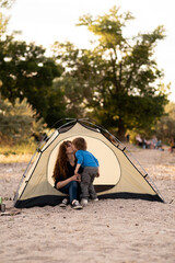 Mother and son sitting in camping tent, admiring sunrise on the river. Family weekend outdoor, local travel on nature, trekking, camp lifestyle.