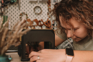 Curly haired woman holds item in desktop laser wood burning machine to inscribe name on surface of...