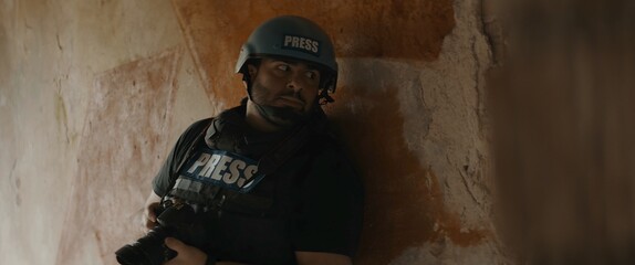 Hispanic male war journalist wearing protective helmet and bulletproof vest gear taking photos during military operation