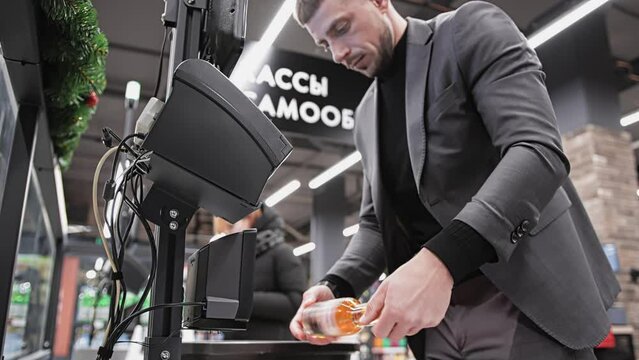 Buyer scans bottle of beer through barcode scanner at self-service checkout ACO in supermarket. Assisted checkout SCO with cashless payment. Shopping at mall and store. Self-checkout