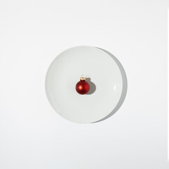 Minimal Christmas composition. Red bauble on white plate. Christmas, winter, new year concept. Flat lay, top view, copy space.