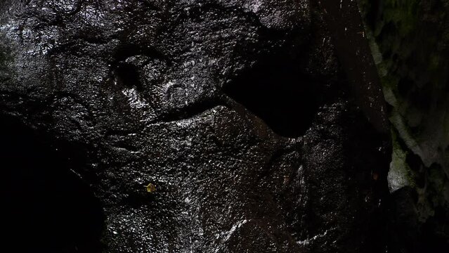 Closeup of a water flowing over dark stone. Dramatic dark waterfall. Dark look with black stones waterfall drops. Dark fantasy waterfall. 