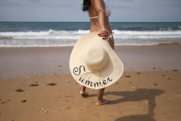 South American woman, young and brunette with bikini and hat with the word summer held in her hand,...