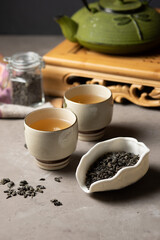 Tea ceremony. Two porcelain cups with green tea, tea leaves in a bowl and a teapot on a tray. Vertical.