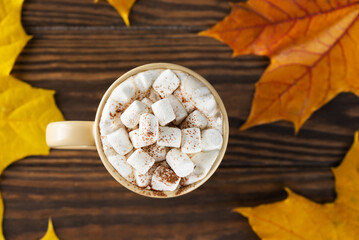 Obraz na płótnie Canvas Hot chocolate drink with marshmallows on a brown wooden table on a background of autumn leaves. Flat lay, top view.