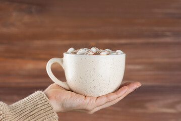 Hot chocolate with marshmallows in a mug in hand.