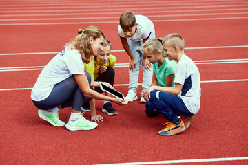 Female coach training athletes. Group of children before running on treadmill at the stadium....