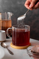 Sugar addiction. Pouring sugar with spoon in cup of tea. Black tea in glass cup. Lifestyle, action...