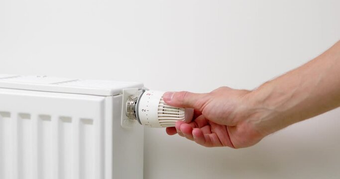 The man turns off the heating by setting the thermostat