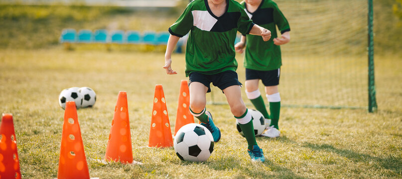 Two school boys running and kicking soccer balls between training cones during slalom drill