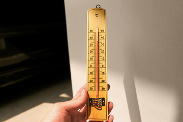 Woman hand holding wooden light brown thermometer measuring or checking temperature degrees of...