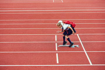 Start. Back to school, kids and education concept. Girl dressed in school uniform as elementary student carrying big backpack running on treadmill at the stadium or arena.