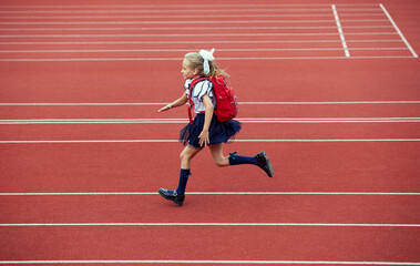 Start. Back to school, kids and education concept. Girl dressed in school uniform as elementary student carrying big backpack running on treadmill at the stadium or arena.