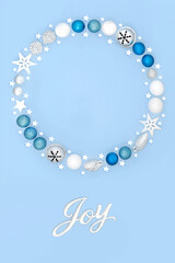 Christmas joy sign with wreath and tree bauble decorations on pastel blue background. Festive fantasy abstract concept for winter Xmas and New Year.