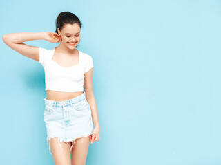 Young beautiful smiling female in trendy summer jeans skirt and top  clothes. Sexy carefree woman posing near blue wall in studio. Positive brunette model having fun.Cheerful and happy