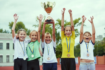Fototapeta premium A boys and girls celebrating a victory. Motivated children team rising hands up. Happy kids playing sports. Concept of win, sport, studying, achievements, success,. teamwork, friendship