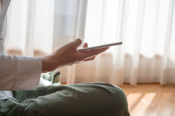 A woman playing with your smartphone by the window in the room.  部屋の窓際でスマホをいじっている女性