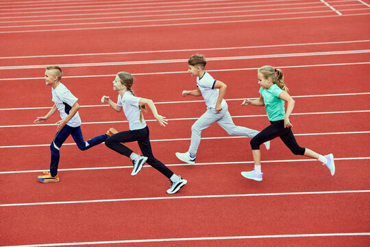 Group of children running on treadmill at stadium or arena. Little fit boys and girls in sportswear training as athletes outdoor. Concept of sport, fitness, achievements, studying, goals, skills