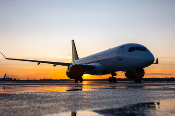 Fototapeta na wymiar Modern passenger jetliner on the airport apron against the backdrop of a picturesque sunset with reflection in a puddle