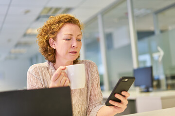 Business Frau im Büro liest Nachricht auf dem Smartphone