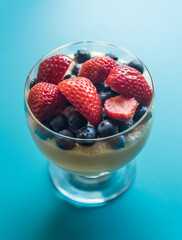Pudding dessert with fresh strawberries and blueberries in a glass bowl