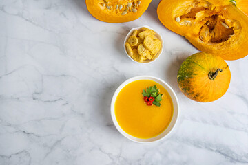 Autumn pumpkin cream soup with pumpkin spices. Delicious and bright vegetarian dish with foodstyling of fresh parsley with hot pepper and seasonings on a white background. Flatlay with copy space text
