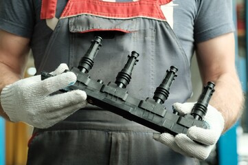 An auto mechanic holds a new induction ignition coil in his hands. Inspection and control of the...