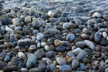 The seashore with lots of pebbles. The sea is on the horizon. A sunny morning day. Background with round stones. The stones on the beach are smooth. View from above.