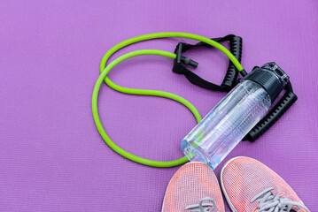 Sneakers, fit tube and a purple fitness mat. Sport concept. Copy-space